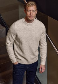 Hellbeige, Wolle Crew-Neck Pullover mit gerippten Bündchen und Saum, kombiniert mit dunklen Jeans. Die Textur wirkt weich und gemütlich.