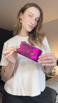 Ροζ μεταλλική θήκη καρτών με υφή λογότυπου, με φερμουάρ και ομαλή επιφάνεια. Κρατιέται στο χέρι ενός ατόμου.