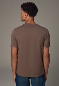 Camiseta marrón de manga corta con cuello redondo, que presenta una textura suave y un diseño simple. Combinada con vaqueros azules.