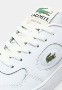 Baskets en cuir blanc avec le logo crocodile vert de Lacoste, bout rond et lacets blancs plats. Détails comprenant des surpiqûres et une languette rembourrée.