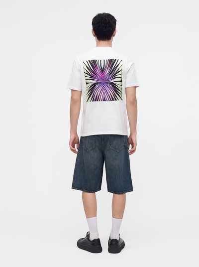 Άνδρας που φοράει λευκό t-shirt με μοβ και μαύρο αφηρημένο σχέδιο στην πλάτη, σκούρα τζιν σορτς, άσπρες κάλτσες και μαύρα αθλητικά παπούτσια.