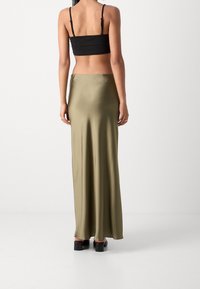 Jupe maxi en satin olive avec une texture lisse, un design fluide et une taille haute. Associée à un haut noir court et des talons épais.