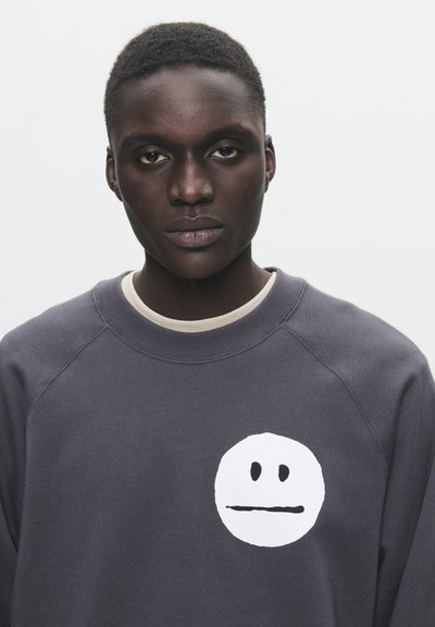 Grauer Sweatshirt aus Baumwollmischung mit einem großen weißen Smiley-Gesicht-Graphic auf der Brust. Gerippter Halsausschnitt und Bündchen, lockere Passform.