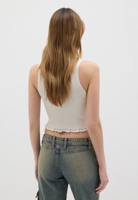 Top corto a coste di un beige chiaro con un orlo a ondina, abbinato a jeans blu sbiaditi a vita alta, che mostrano una vestibilità rilassata e una texture morbida.