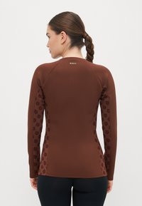 Ruda ilgaa, ilgomis rankovėmis rashguard palaidinė su gėlių raštu ant rankų, prigludęs dizainas, minkšta tekstūra, su 'ROXY' logotipu šviesiai žalia spalva ant nugaros.