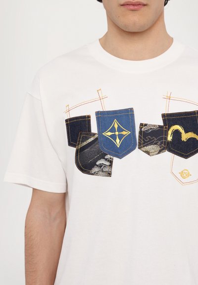 T-shirt en coton blanc présentant un graphique de cinq poches dans différentes textures de denim, avec des accents bleus et noirs et des détails de couture dorés.