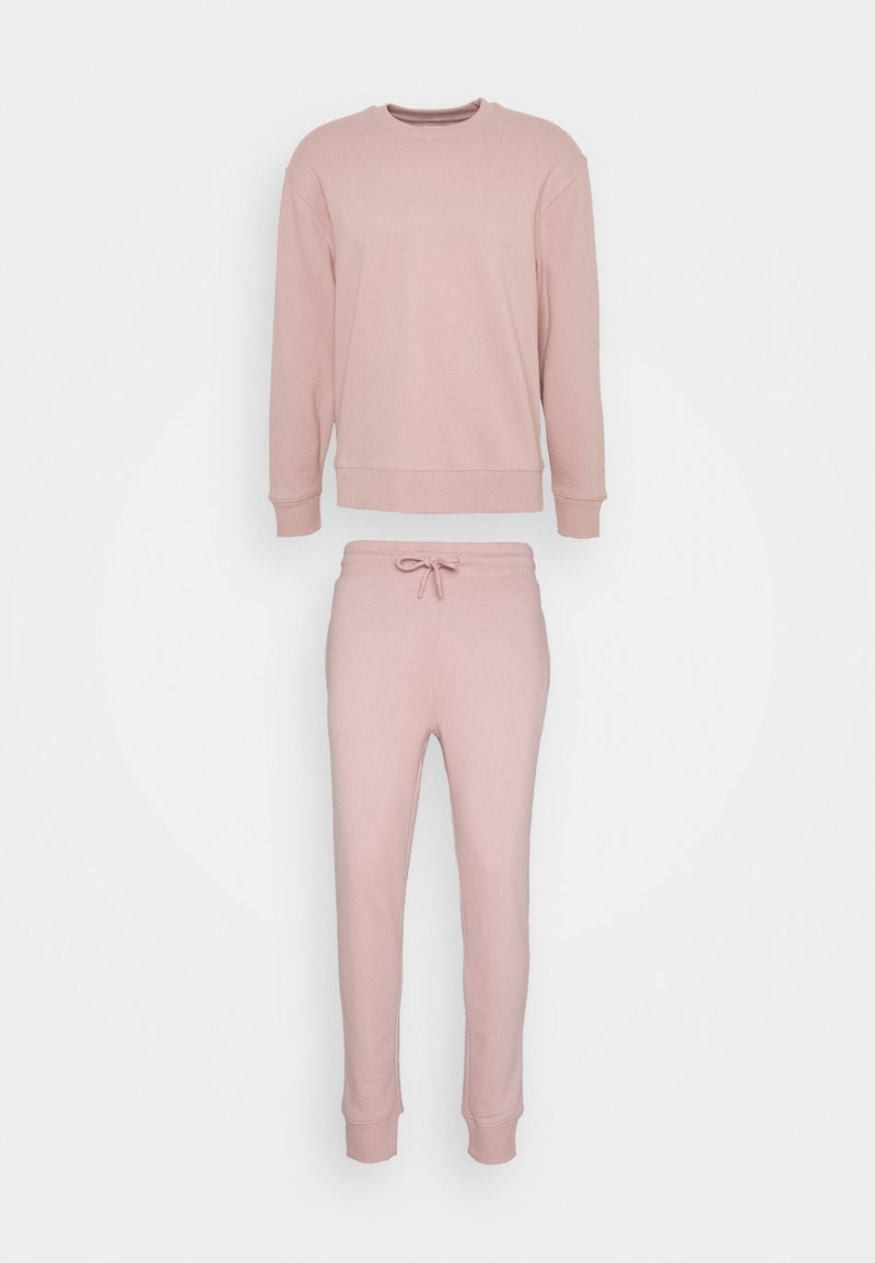 Sweat-shirt à manches longues rose pâle et pantalon de jogging assorti avec taille à cordon et poignets côtelés, disposés à plat sur fond blanc.