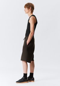 Un top negru fără mâneci, asociat cu pantaloni scurți de culoare verde măslin. Pantalonii scurți au buzunare laterale și un elastic la talie cu șnur. Adidași negri cu talpă de cauciuc.