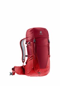 Red backpack with a textured exterior, adjustable straps, padded back panel, and side pockets. Features a top loading design and reflective logo.