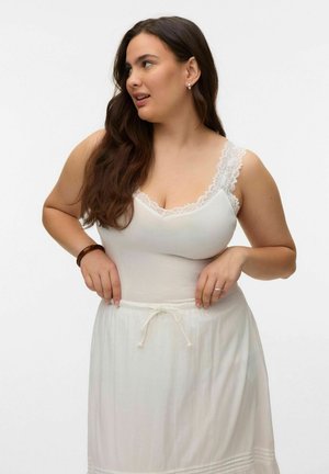 Woman with long brown hair wearing a white lace-trimmed tank top and white drawstring skirt, looking to her left.