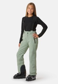 Skihosen in Hellgrün mit verstellbaren schwarzen Trägern, seitlichen Reißverschlüssen und verstärkten schwarzen Knöchelbesätzen, getragen mit schwarzen Skischuhen.