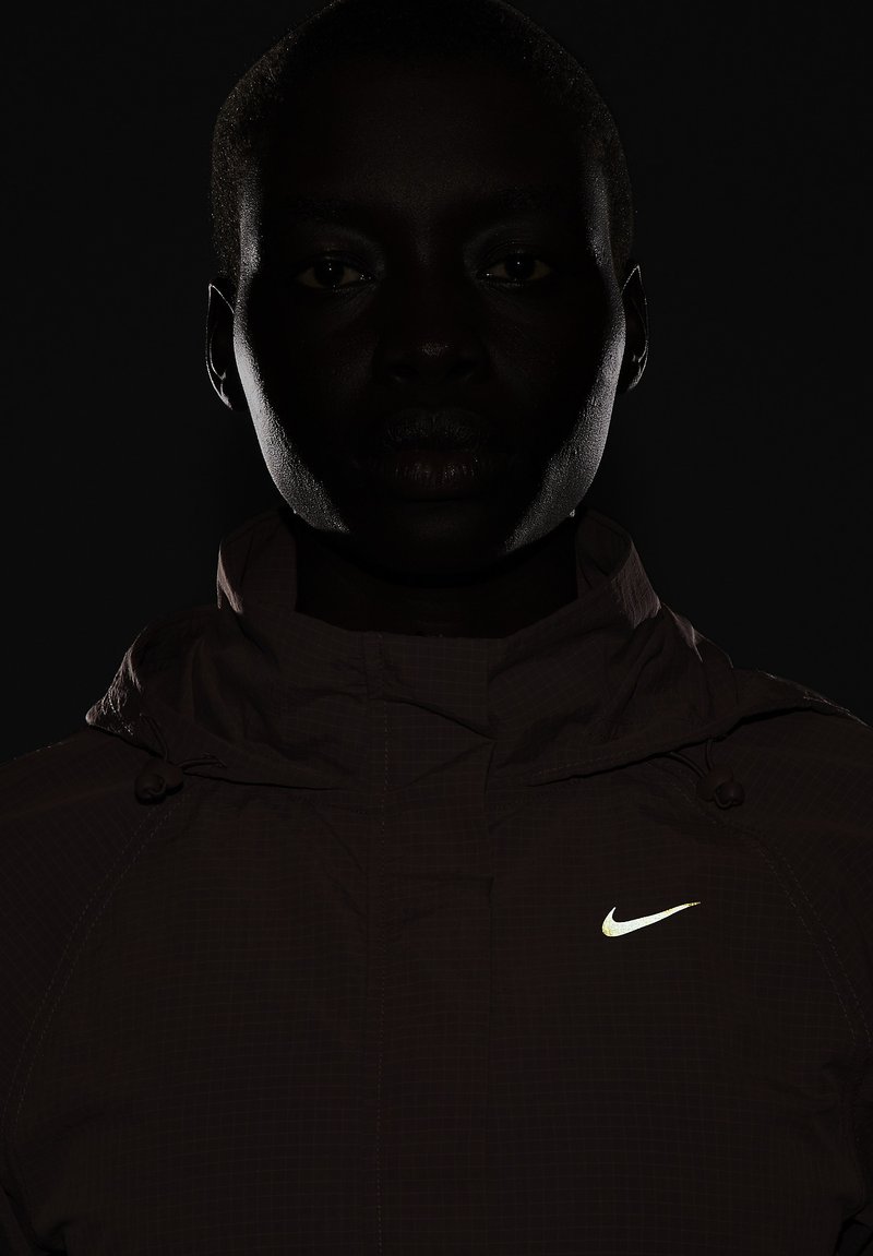 Nike capuchonjack in donkerbruin, met een gestructureerd oppervlak, reflecterend logo en verstelbare toggles op de capuchon en kraag.