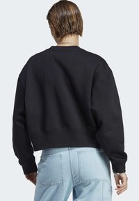 Black cropped sweatshirt with dropped shoulders and ribbed cuffs, paired with light blue cargo jeans featuring double back pockets.