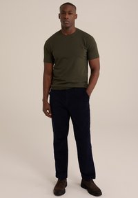 Tričko s krátkým rukávem olivově zelené barvy, kombinované s námořnickými kordurovými kalhotami a hnědými šněrovacími botami. Hladká textura a přiléhavý střih.