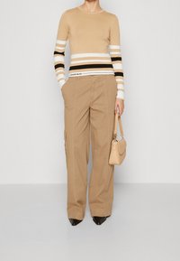 Haut à rayures beiges à manches longues avec des bandes noir et blanc ; pantalon cargo tan ample ; sac à main marron clair ; escarpins noirs à bout pointu.