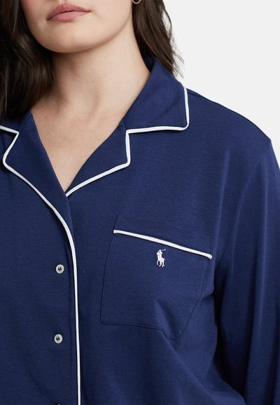 Cămașă de pijama bleumarin, cu detalii din piping alb, un buzunar pe piept și un mic logo brodat. Fabricată dintr-un material moale, cu o croială lejeră.