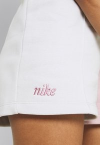 Bílé bavlněné šortky s růžovým vyšívaným logem „nike“ na lemu, s hladkou strukturou a jednoduchým designem.