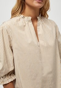 Beige gestreifte Bluse mit Stehkragen, plissiertem Ausschnitt und puffärmel mit elastischen Bündchen, aus einem leichten Stoff gefertigt.