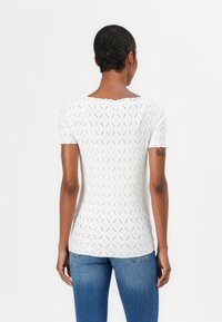 Top bianco a maniche corte con un motivo a diamante testurizzato, design aderente e scollatura ampia, abbinato a jeans blu.