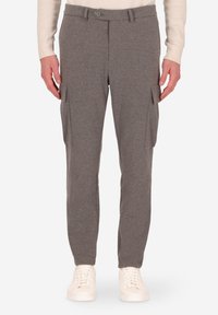 Uomo che indossa pantaloni cargo grigi con tasche laterali e sneakers bianche, in piedi su uno sfondo bianco.