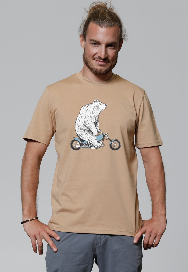 Beige t-shirt met een graphic van een beer die op een blauwe fiets rijdt. Korte mouwen en een relaxte pasvorm, gemaakt van zachte katoen.