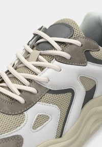 Béžové sieťované a šedé semišové tenisky s bielymi akcentmi, okrúla špička, textúrovaný zvršok a ploché šnúrky. Pozoruhodný dizajn s vrstvenými panelmi.