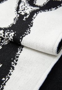 Black and white patterned knit scarf with a soft texture, featuring a contrasting design and rolled edges.
