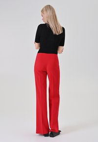 Pantaloni rossi a vita alta con taglio a gamba dritta, abbinati a un top nero aderente a maniche corte. Tessuto liscio con finitura elegante.