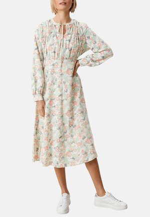 Robe midi à imprimé floral dans des couleurs pastel légères, avec un col froncé, des manches longues et une taille cintrée. Associée à des baskets blanches.
