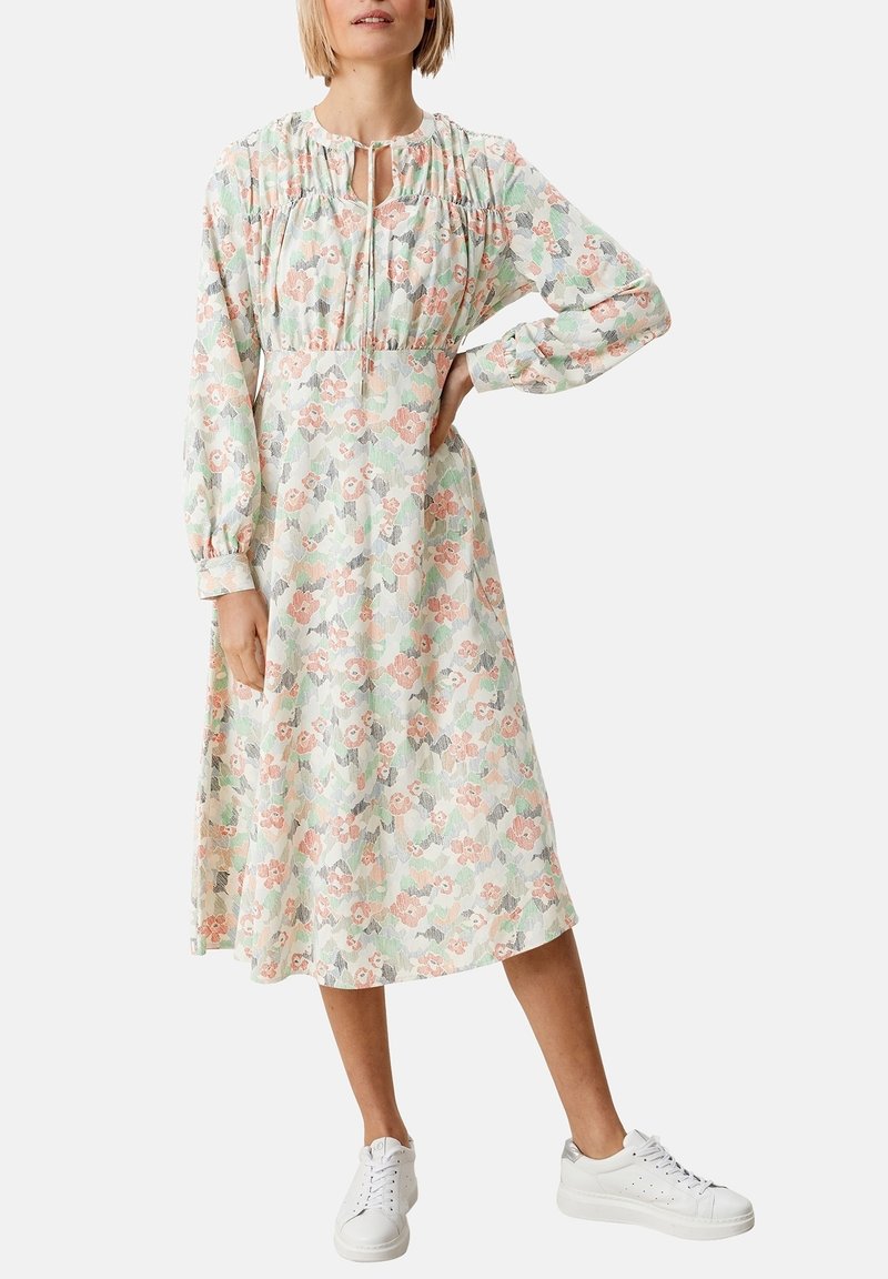 Blommig midi-klänning i ljusa pastellfärger, med rynkad halsringning, långa ärmar och åtdragen midja. Matchas med vita sneakers.