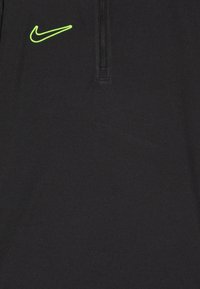 Sort atletisk top med kvart-zip hals. Har et neon grønt Nike-logo på venstre bryst. Glat tekstur med en tætsiddende silhuet.