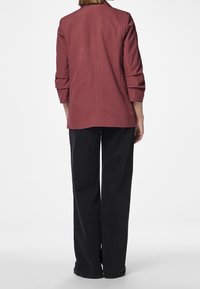 Veston bordeaux à coupe ajustée, à manches trois-quarts et ourlet droit, associé à un pantalon large noir, présentant une texture lisse.