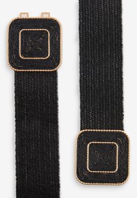 Sangle noire tissée avec des accents carrés. Les accents présentent une bordure dorée tressée, créant un motif géométrique texturé.