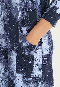 Blau- und grau gemustertes Kleid mit Dreiviertelärmeln, das eine Seitentasche und eine weiche, glatte Stofftextur aufweist.