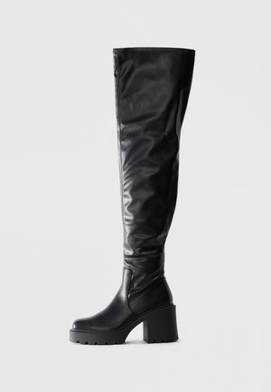 Black over-the-knee boots made of smooth leather, featuring a chunky platform heel and seam detailing along the shaft.