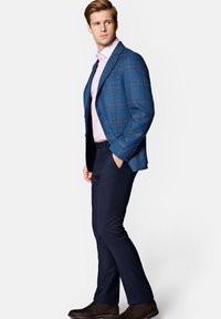 Niebieska marynarka w kratę na jasnoróżowej koszuli, w połączeniu z ciemnoniebieskimi spodniami i ciemnobrązowymi butami. Gładki materiał o strukturalnym kroju.