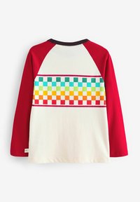 Langærmet T-shirt i creme med røde raglanærmer. Har et flerfarvet ternet mønster på ryggen. Blødt bomuldsstof.