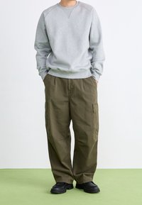 Grauer Sweatshirt mit gerippten Bündchen und Rundhalsausschnitt, kombiniert mit locker sitzenden olivgrünen Cargo-Hosen mit Taschen. Schwarze klobige Schuhe.