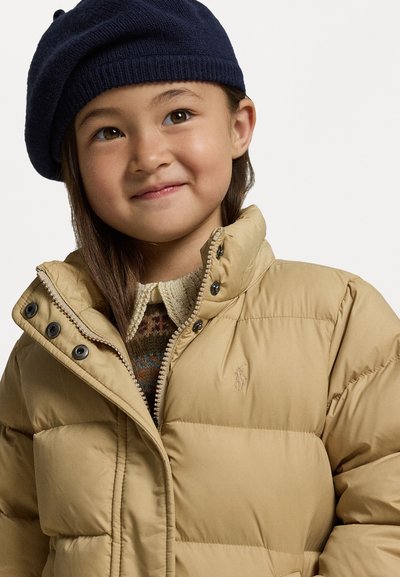 Puffete beige jakke med høy krage og knappefront, kombinert med en strikket genser og en mørk marineblå beret.