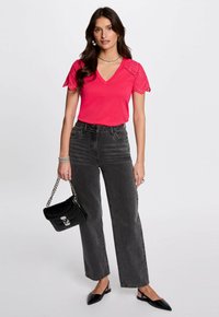 Top fucsia de cuello en V con mangas de encaje, combinado con unos vaqueros de pierna ancha negros de cintura alta. Los accesorios incluyen un pequeño bolso negro y unos zapatos planos elegantes.
