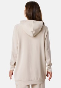 Beige hoodie met een grote, zachte capuchon, lange mouwen en geribbelde zoom. De stof lijkt glad en comfortabel, geschikt voor casual kleding.