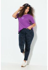 Fialové tričko s kulatým výstřihem a grafikou růže, v kombinaci s tmavými džíny s květinovým vzorem. Model má na sobě bílé tenisky.