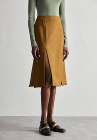 Brun herringbonekjol med framficka, skräddarsydd passform och sidofickor. Matchad med svarta loafers med en guldkedjeaccent.