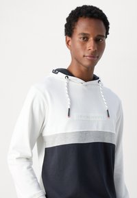 Felpa con cappuccio, parte superiore bianca, fascia centrale grigia e pannello inferiore blu navy. Presenta lacci e etichetta frontale con coordinati.
