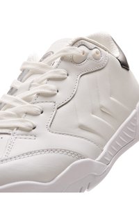 Vit sportskor med en slät läderöverdel, framträdande sömmar, rund tå, platta vita snören och en texturerad gummisula med spår.