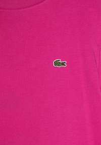 T-shirt di cotone fucsia con scollatura a girocollo e maniche corte, caratterizzato da un piccolo logo di un coccodrillo ricamato in verde sul petto.