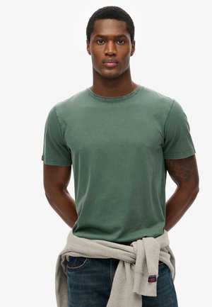 Groene katoenen T-shirt met ronde halslijn en korte mouwen. Bevat een grijze trui die om de taille is geknoopt. Eenvoudig en strak ontwerp.