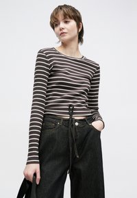 Brūni un balti svītrains garām piedurknēm īss tops ar apaļu izgriezumu un auklu viduklī, kombinēts ar tumšām augsta vidukļa džinsām.