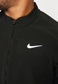 Black athletic jacket with a zip closure and high collar. Features a white Nike logo on the chest and smooth, lightweight fabric texture.