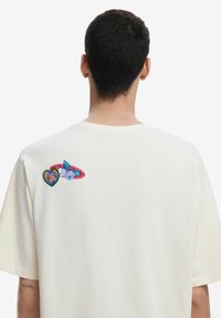 T-shirt di cotone crema con un colorato design ricamato di cuori e foglie sulla schiena, dalla vestibilità rilassata e maniche corte.